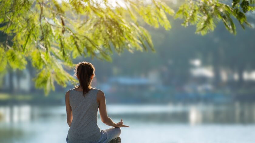 Schöne Frau praktiziert Yoga am Wasser im Park.